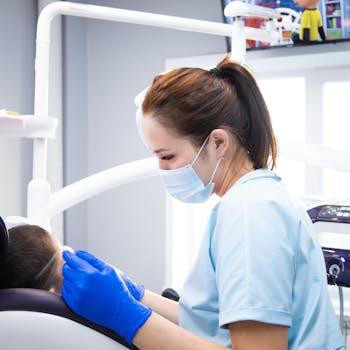 pexels-photo-9951388-9951388 A female dentist wearing gloves and a mask attends to a patient in an indoor clinic setting.